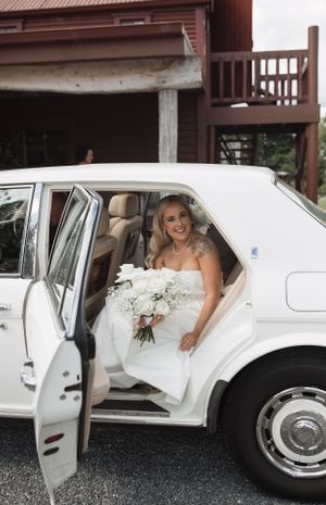 A classic white limousine with wedding decorations parked outside a rustic building.