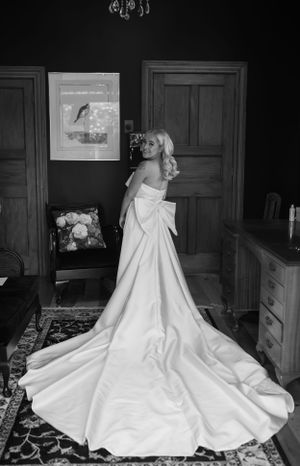 Elegant white wedding dress with long train displayed on dark hardwood floor.
