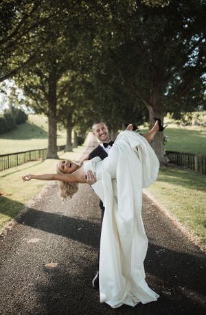Couple performs romantic dip pose on tree-lined path during sunset photoshoot.