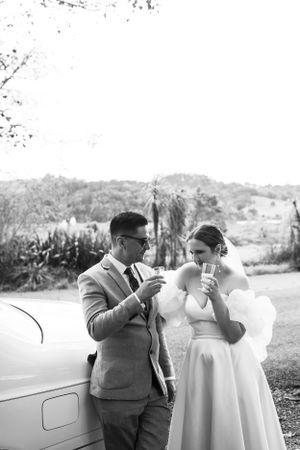 A vintage-inspired black and white photo of a couple enjoying drinks beside a classic car.
