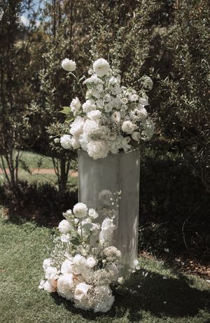 Lush white floral arrangements with peonies and baby's breath in modern vases outdoors.