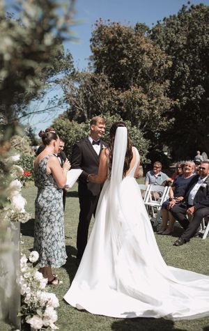Outdoor wedding ceremony in progress with floral arch decorations and seated guests.
