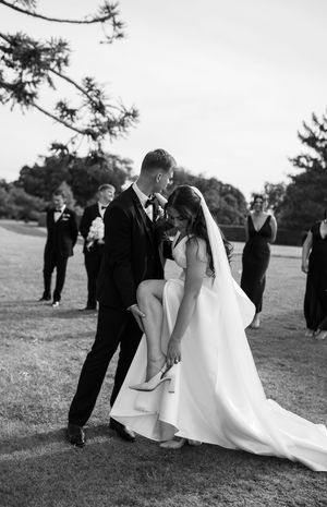 A black and white wedding photo series showing a couple sharing intimate moments outdoors with guests in the background.