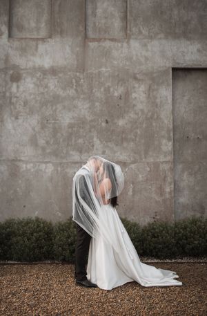 A haunting artistic photo series shows a white flowing fabric creating ghostly shapes against a concrete wall and gravel ground.