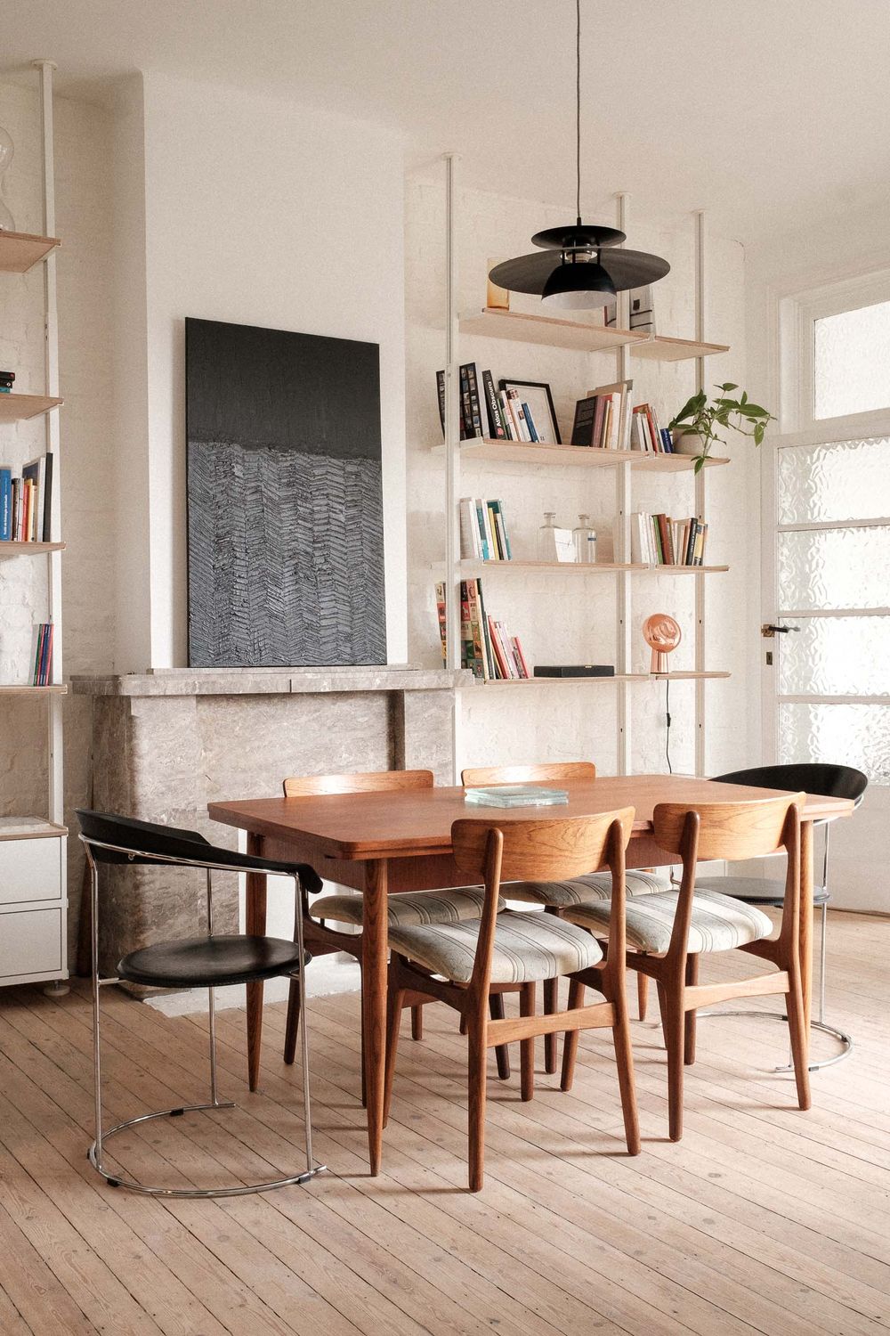 Mid-century modern dining room with wooden table, floating shelves, and large abstract artwork.