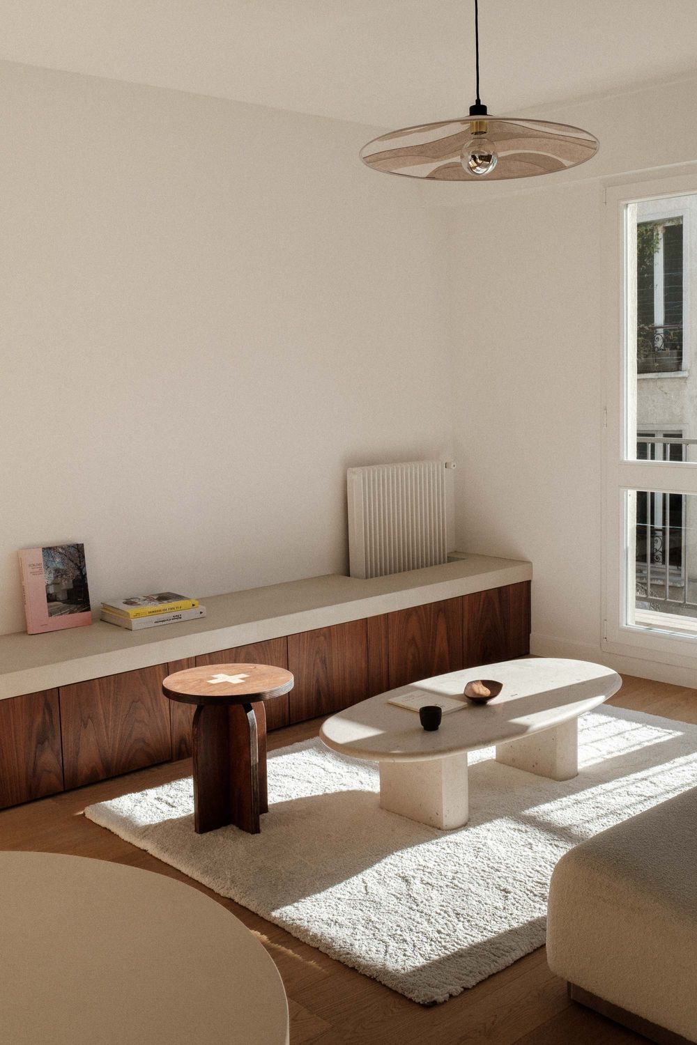 Sunlit living room with wooden bench seating and sculptural coffee tables on white rug.