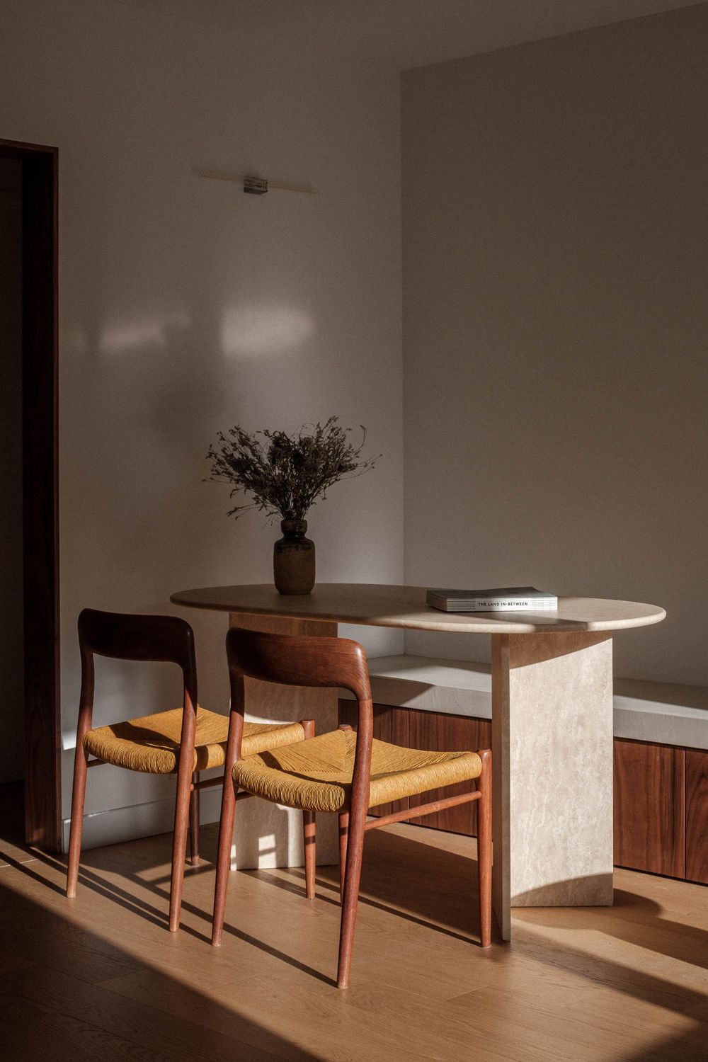 Modern dining area with wooden chairs and marble table bathed in natural sunlight.