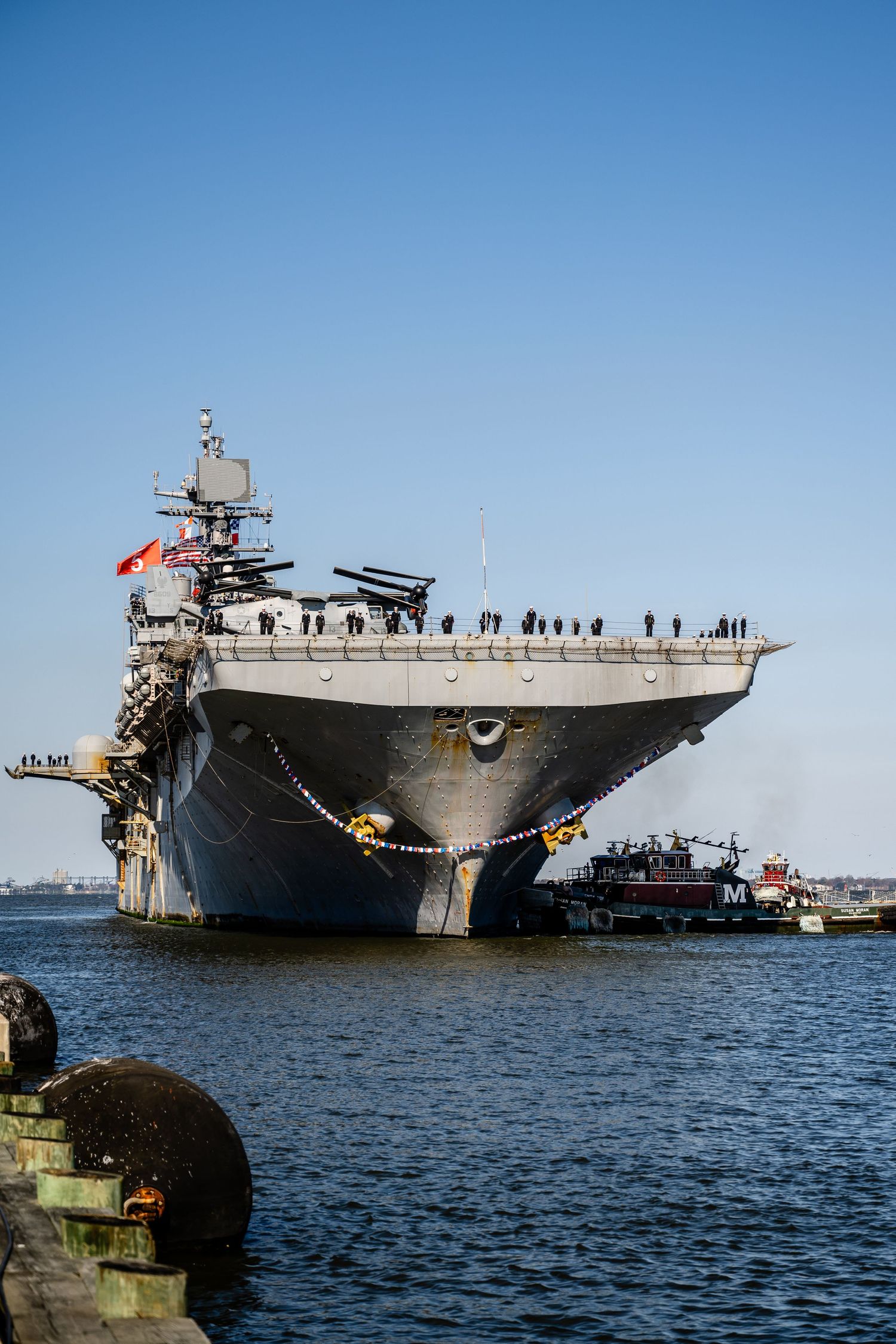 Aircraft carrier  at port with sailors lined up on deck against blue sky.