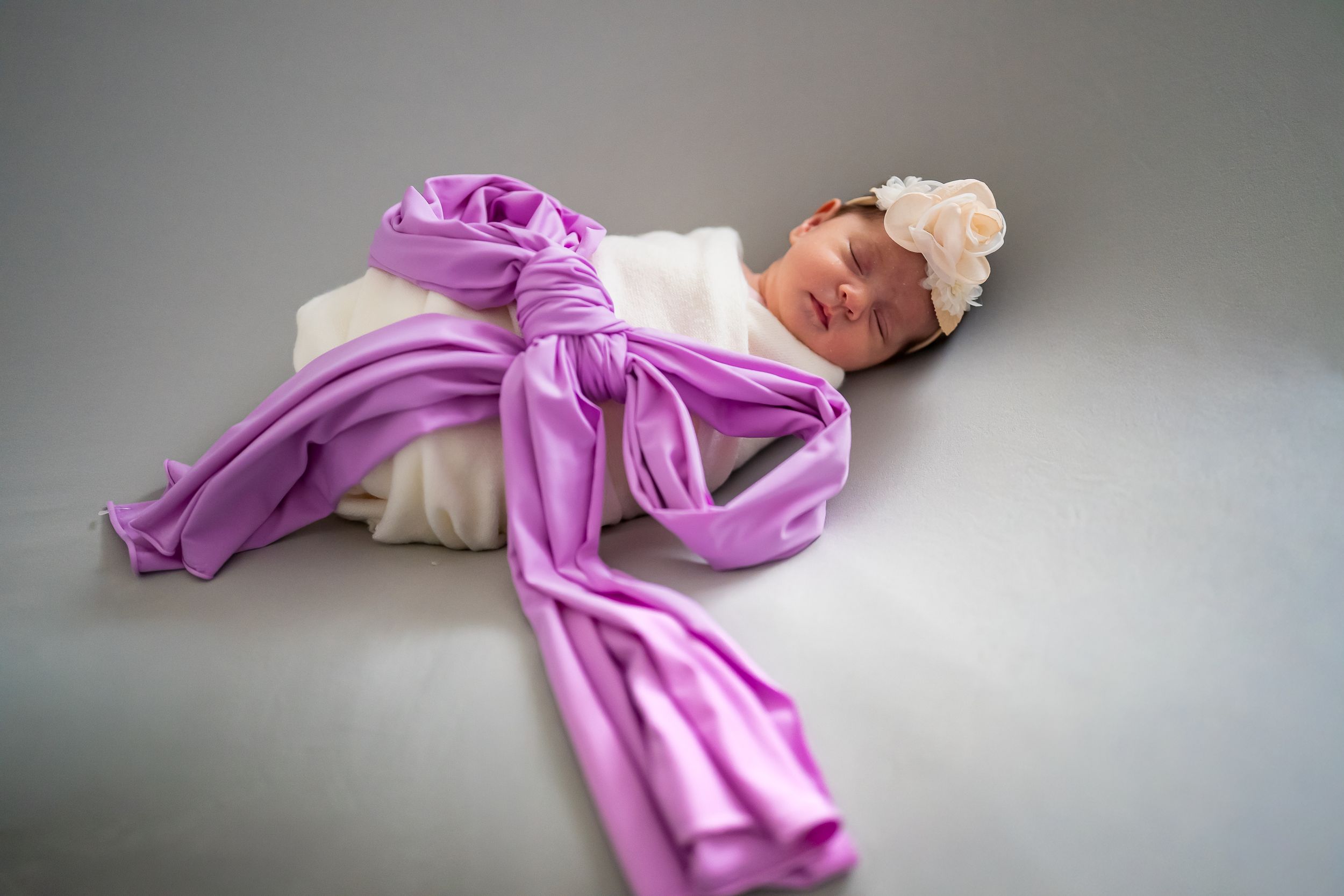 A flowing purple silk fabric gracefully drapes and billows against a neutral gray background.