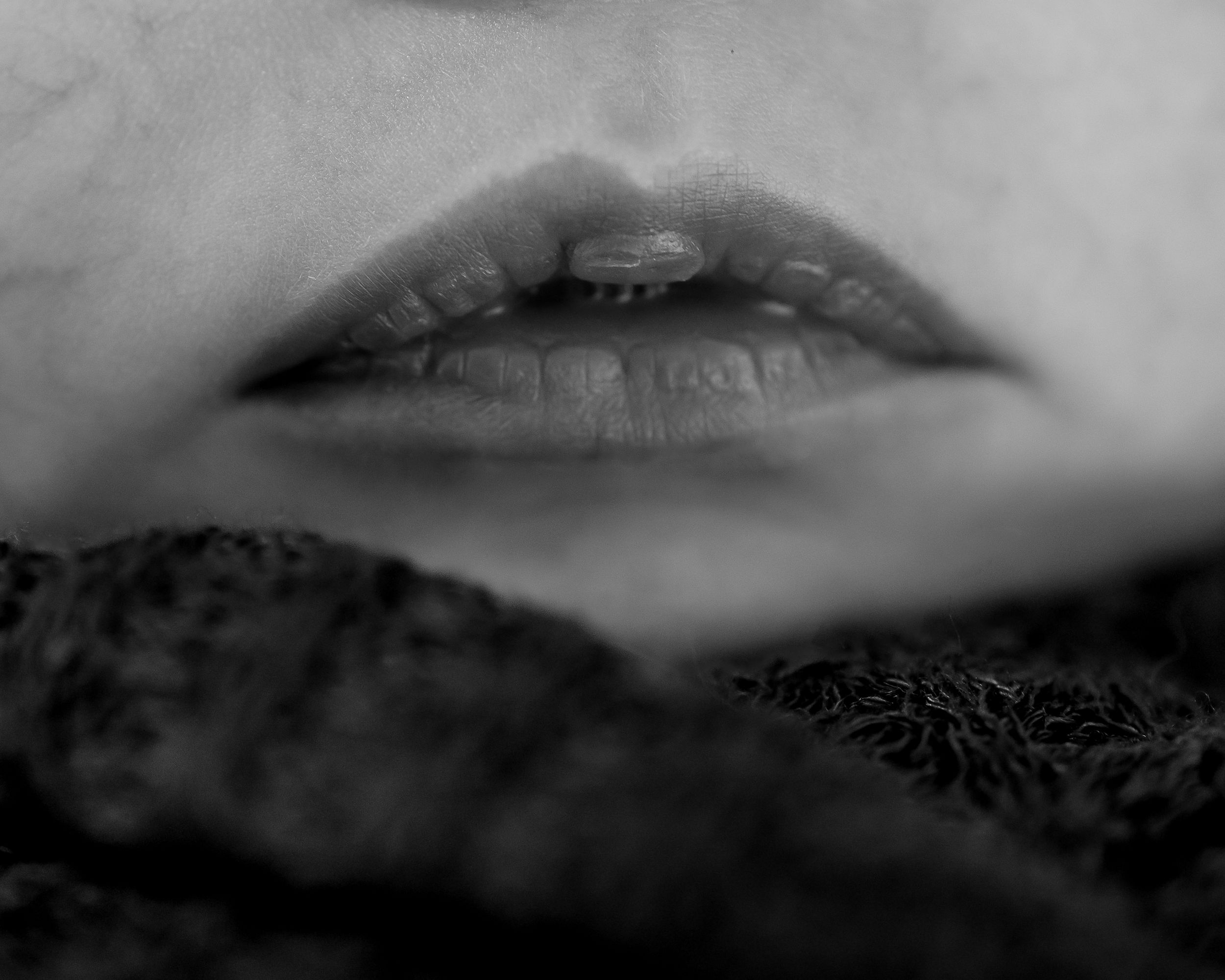 Close-up black and white photo of full lips resting on dark textured fabric.
