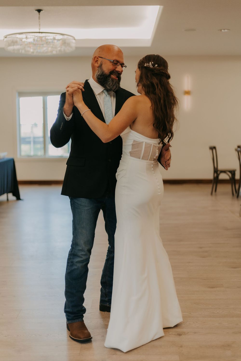 A couple shares an intimate dance moment in a spacious ballroom with light wood floors and cream-colored walls.