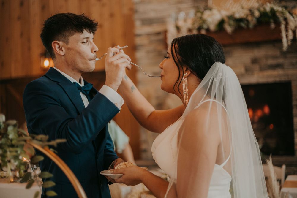 Newlyweds share a playful moment during their first bite of cake at a rustic wedding reception.