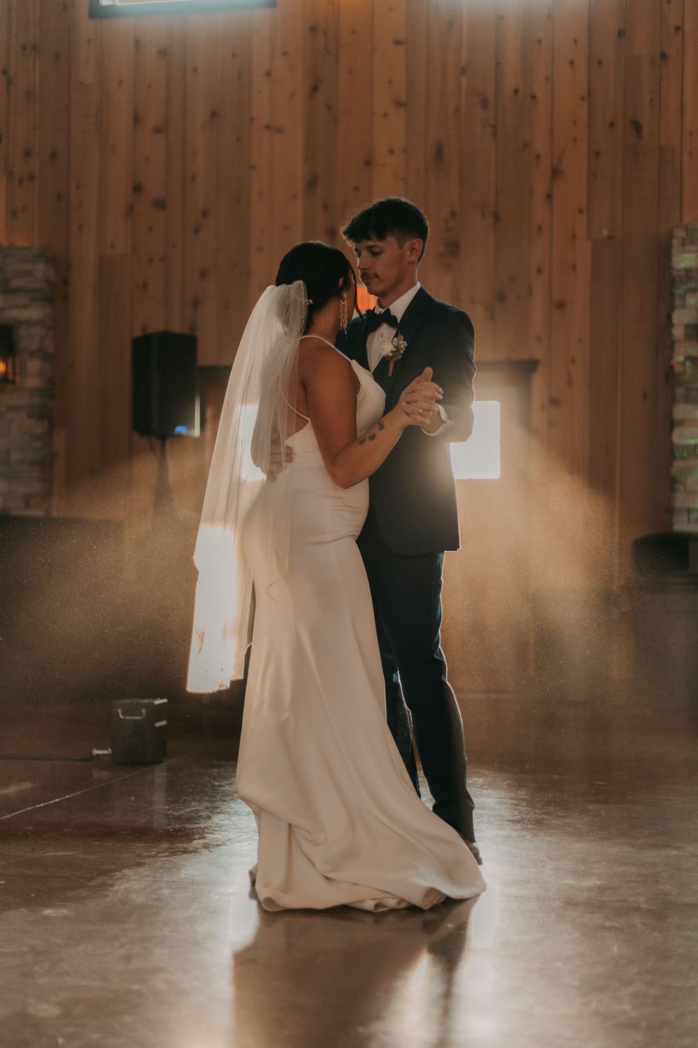 An intimate wedding dance moment captured in a rustic barn reception venue with wooden walls.