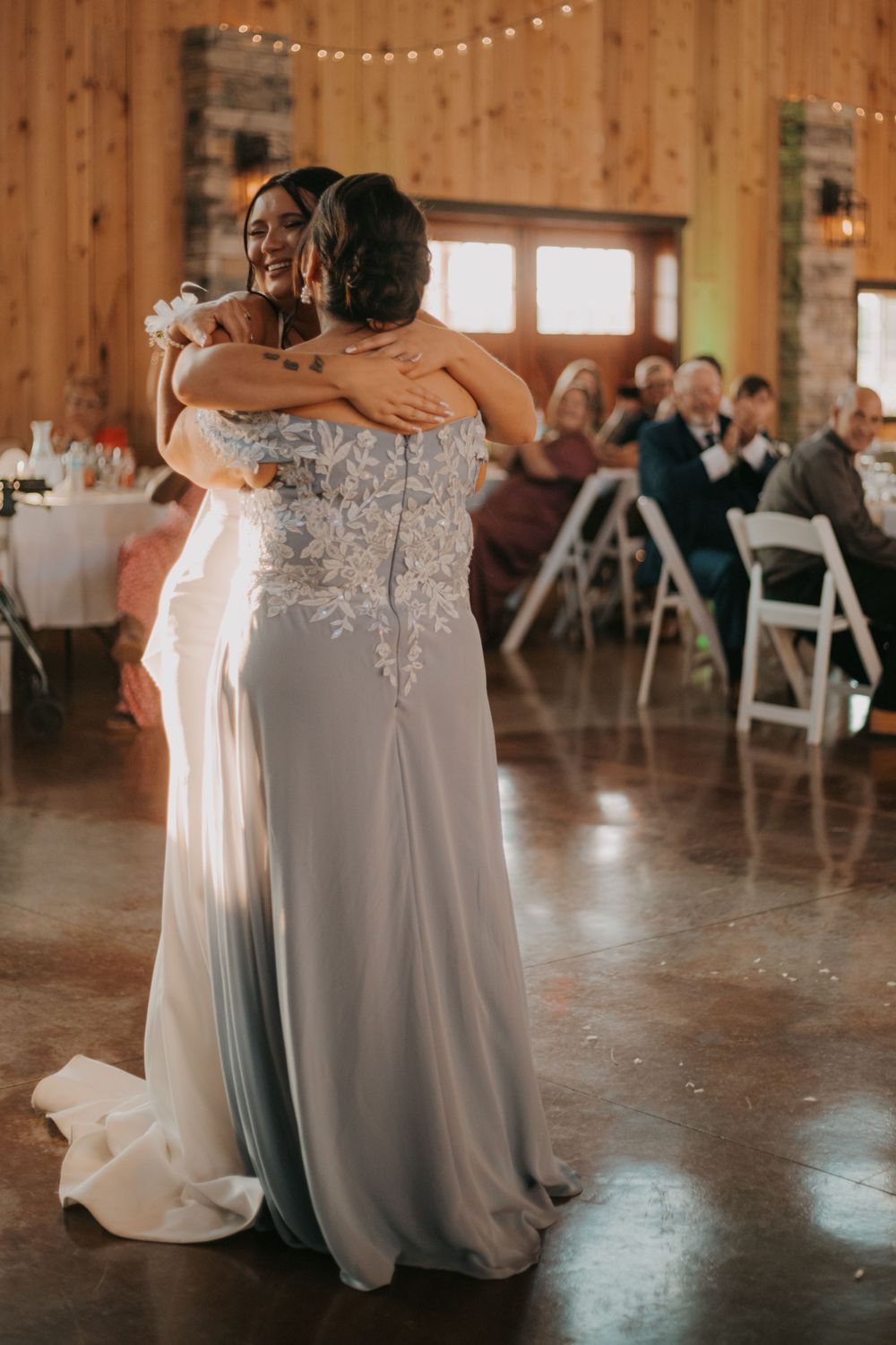 Two people dance and embrace during a wedding celebration in a rustic wooden barn venue.