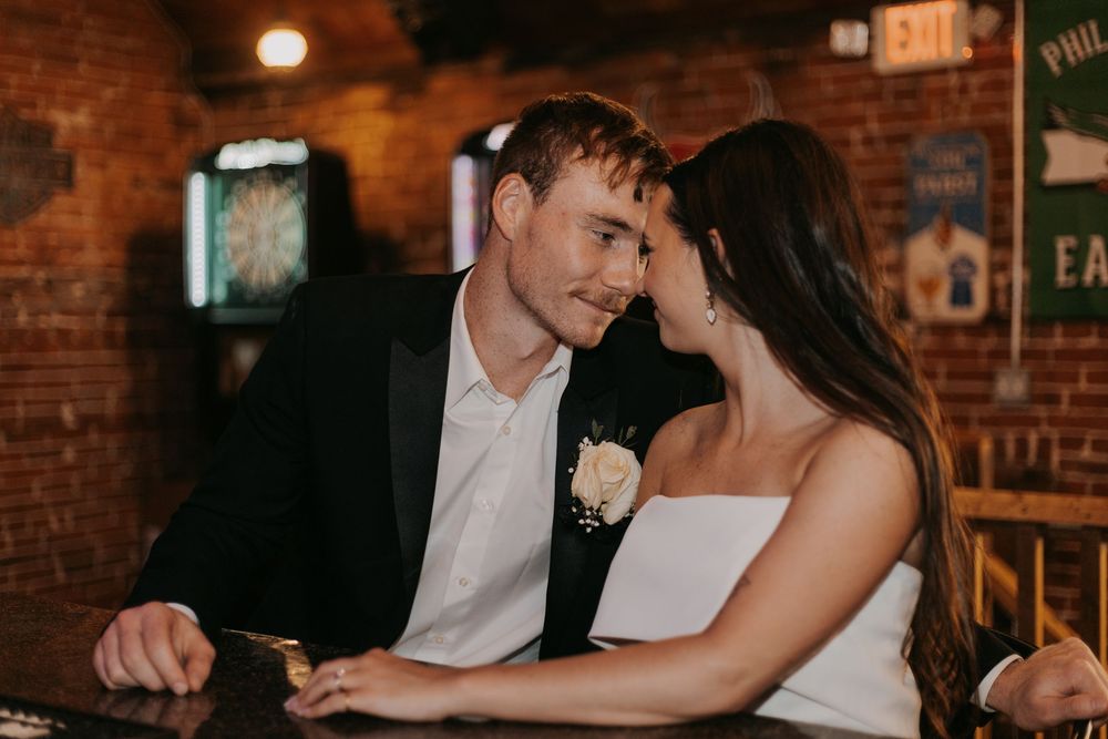 Romantic couple in formal attire share an intimate moment at a rustic brick-walled bar or restaurant.