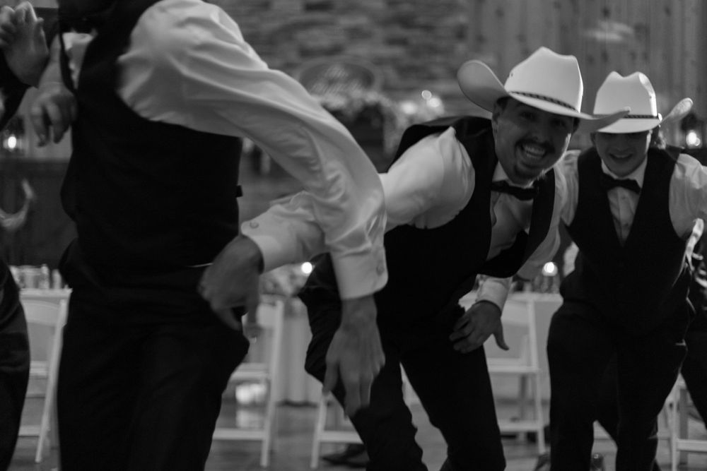 Group of guests in cowboy hats perform line dance at wedding celebration.