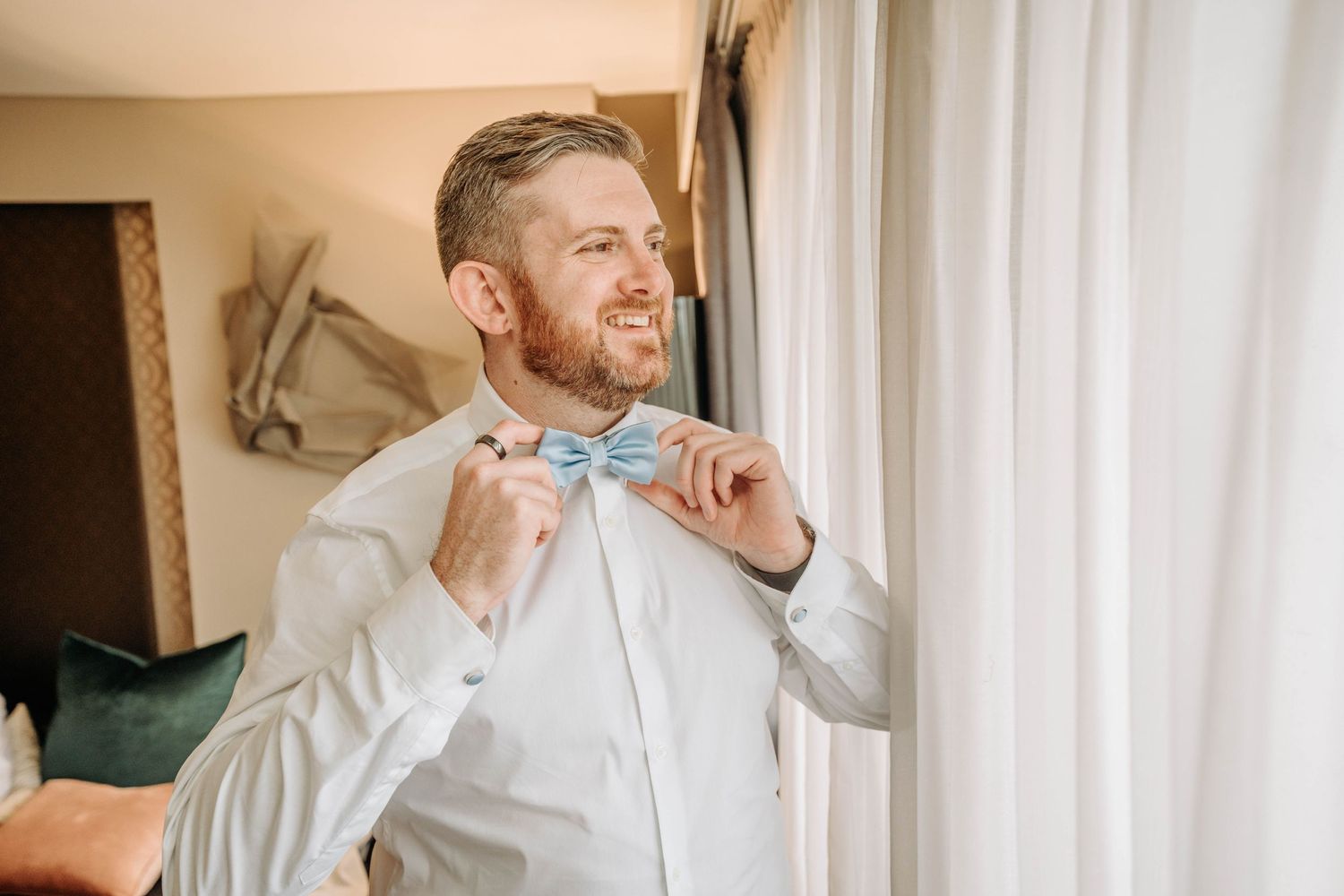 Groom adjusts his light blue bowtie while getting ready on his wedding day.