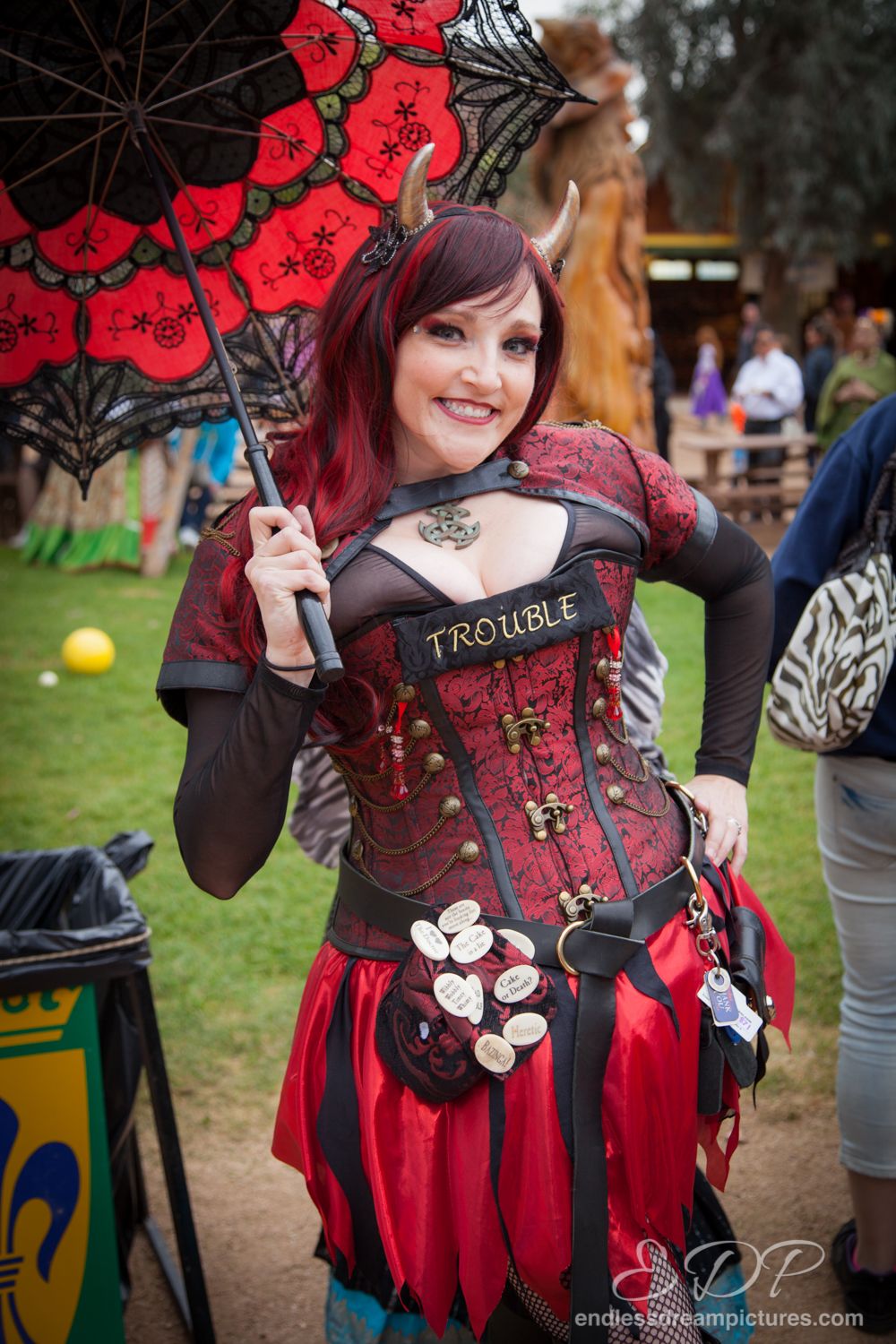 Woman in gothic red and black costume holding decorative parasol at outdoor event.