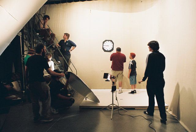 Film crew working on a video production set with lighting and equipment in studio.