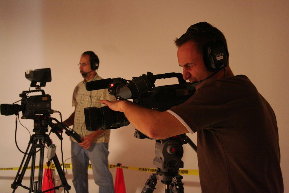 Two camera operators filming with professional video equipment in a studio setting.