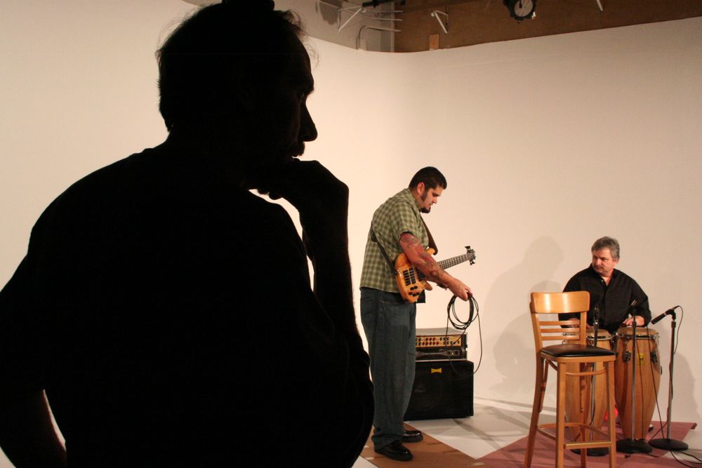 Silhouetted figure watching musicians perform in studio setting.