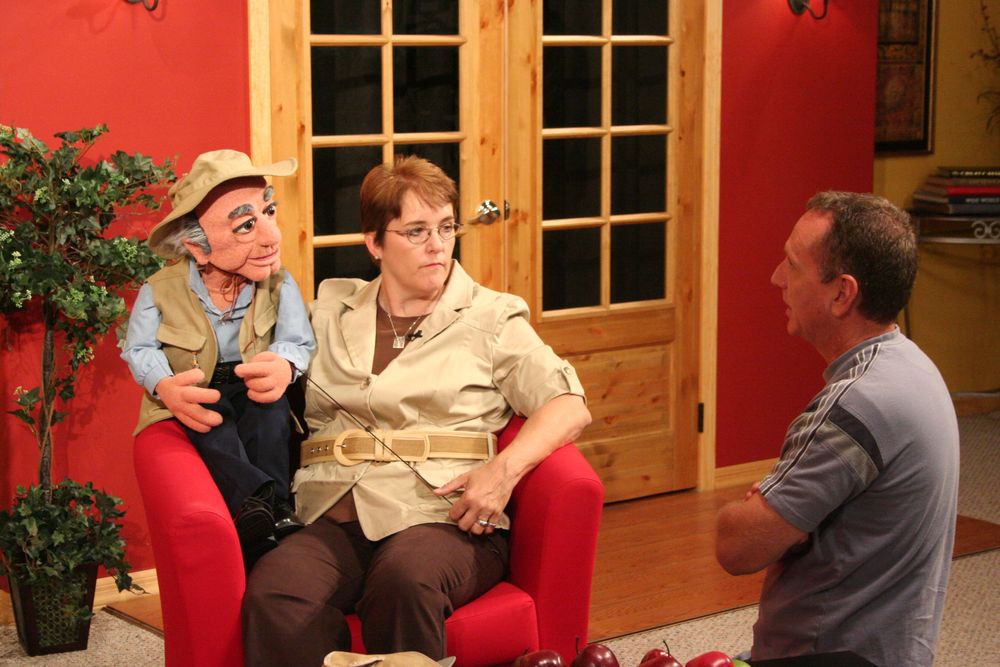 Television interview setup with guests seated on a red couch in a living room setting.