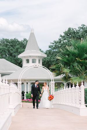 A couple walks along an elegant white gazebo-lined walkway with palm trees and greenery in the background at Disney World.