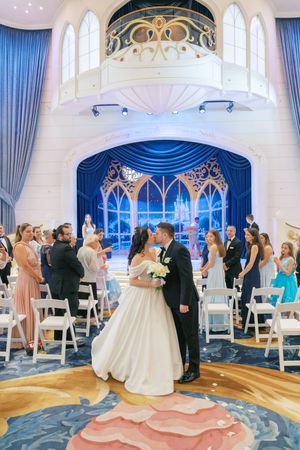 A wedding ceremony in a Disney-themed chapel with blue curtains and ornate gold details on the ceiling and archways.