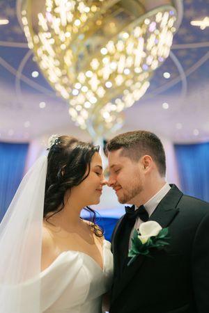Romantic wedding couple shares intimate moments under sparkling crystal chandeliers in an elegant blue-lit ballroom.