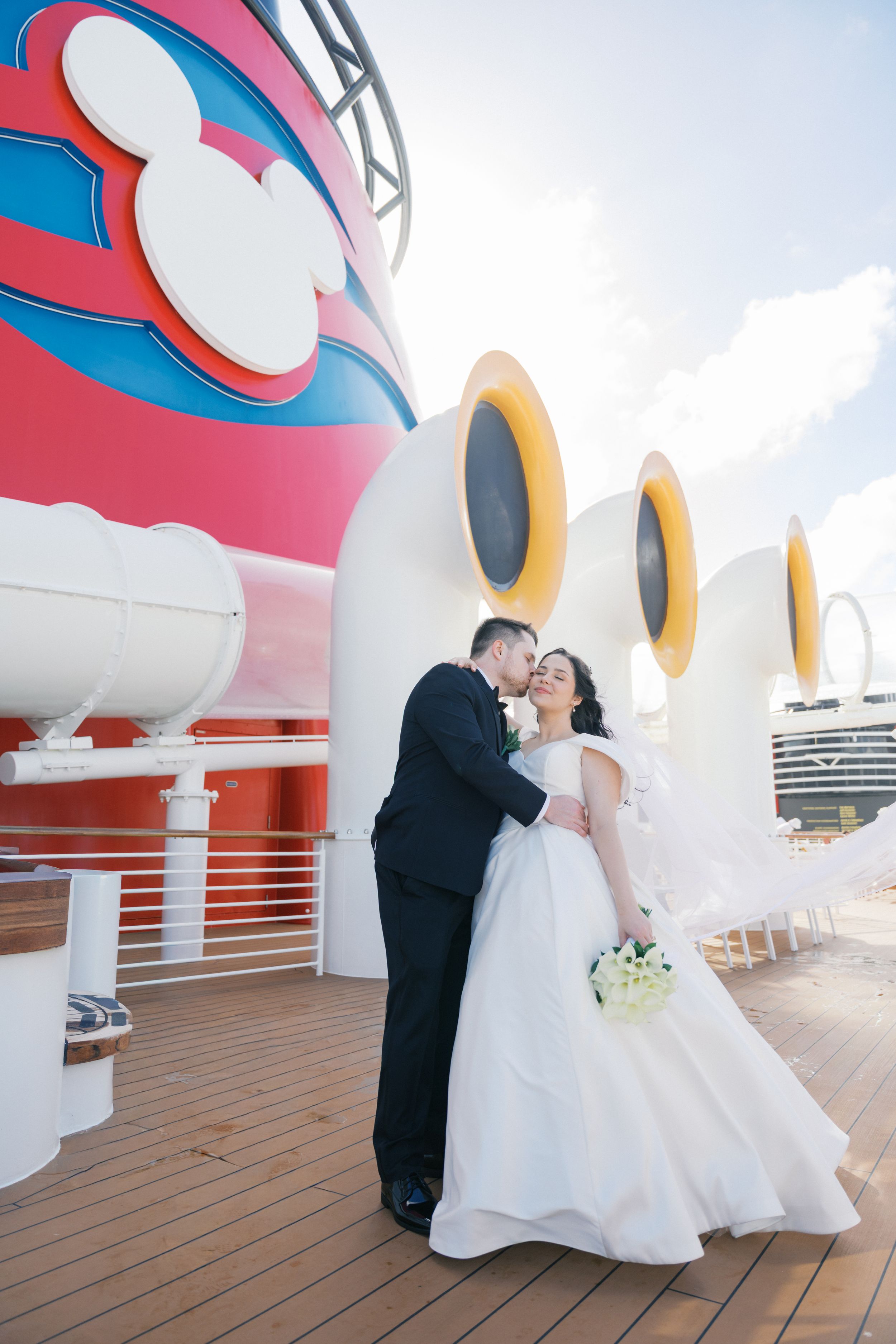 A wedding photo on the deck of a Disney cruise ship with the iconic Mickey Mouse logo visible in the background.