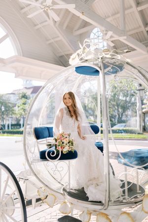 A white ornate horse-drawn carriage with blue velvet seats and floral decorations sits in a bright sunlit venue.
