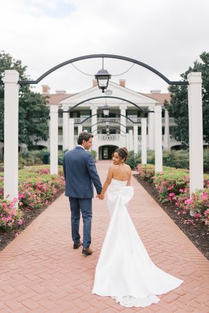 A romantic stroll down a brick pathway lined with pink roses and white columns beneath an elegant arched pergola.