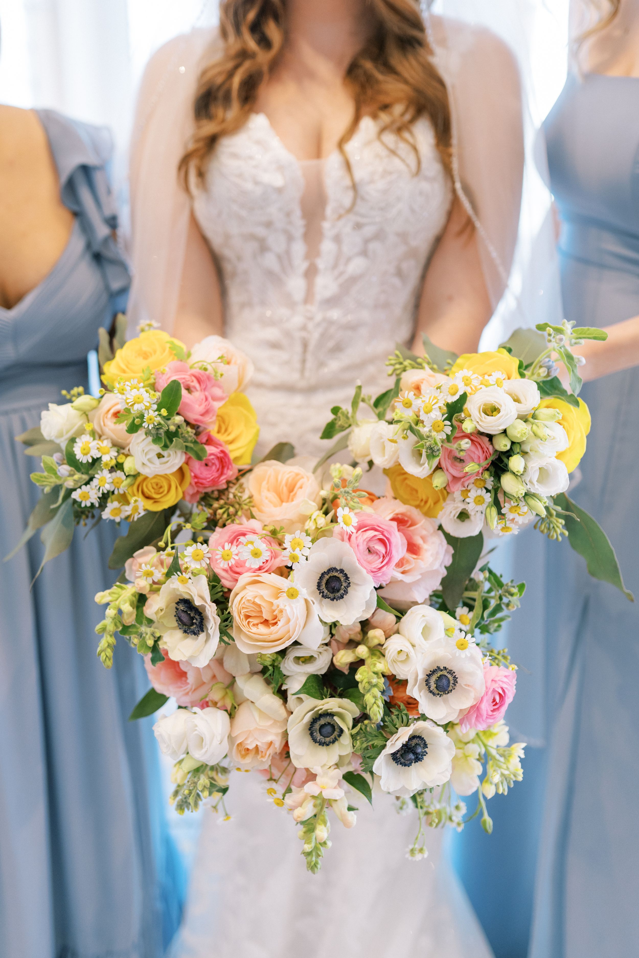 Wedding party holds pastel bouquets with roses, anemones and mixed flowers against powder blue bridesmaid dresses.