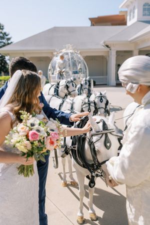 A couple admires decorative white horse-drawn carriage harnesses outside an elegant wedding venue.