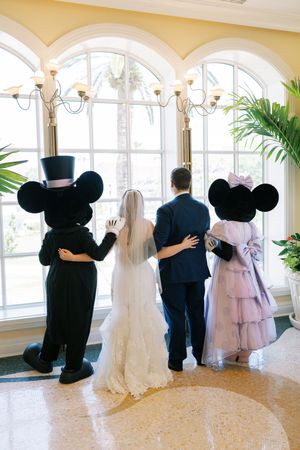 Wedding couple and Disney characters Mickey and Minnie Mouse look out arched windows in elegant venue.