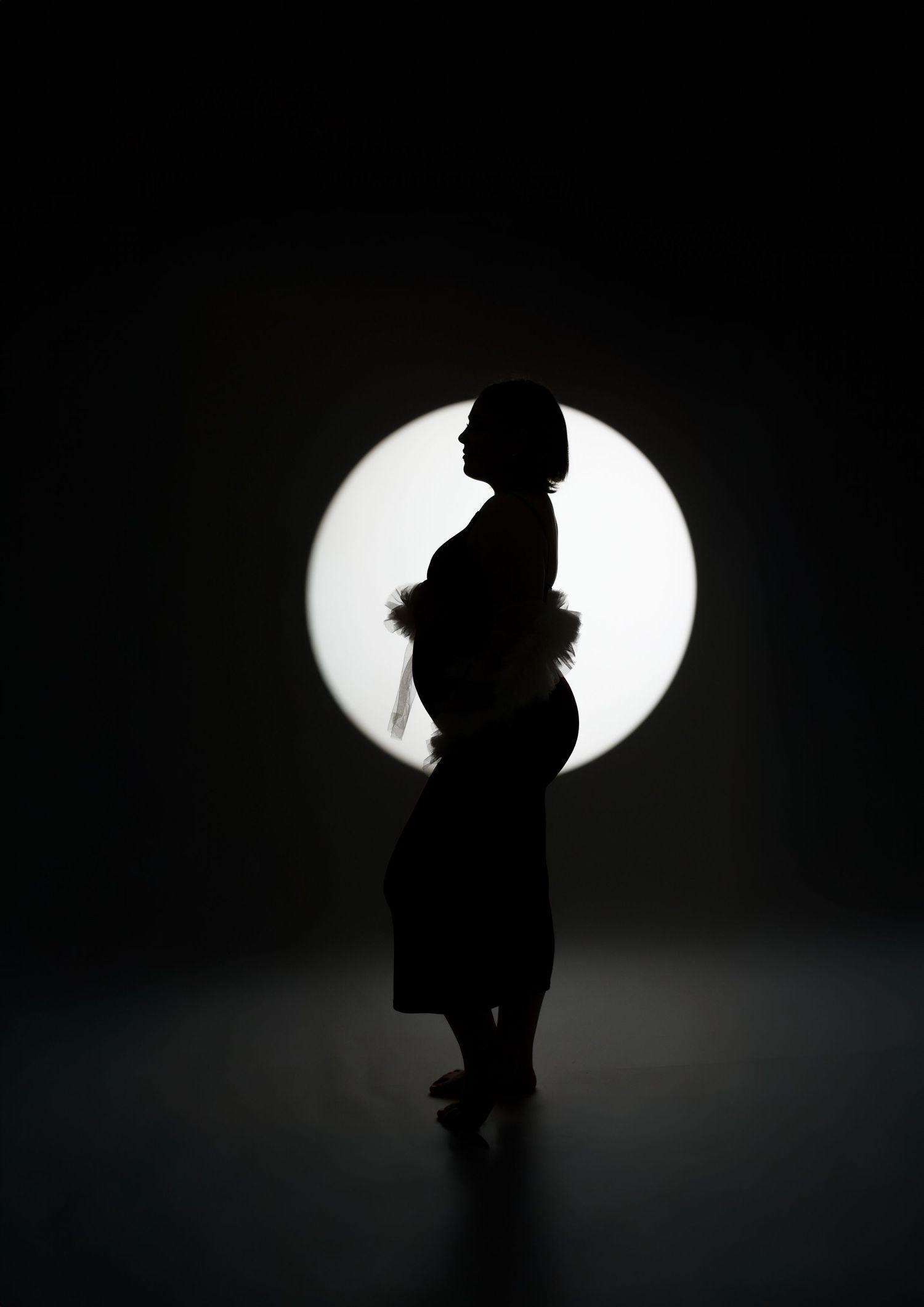 A woman in a black evening gown poses elegantly on a white surface against a dark dramatic background.