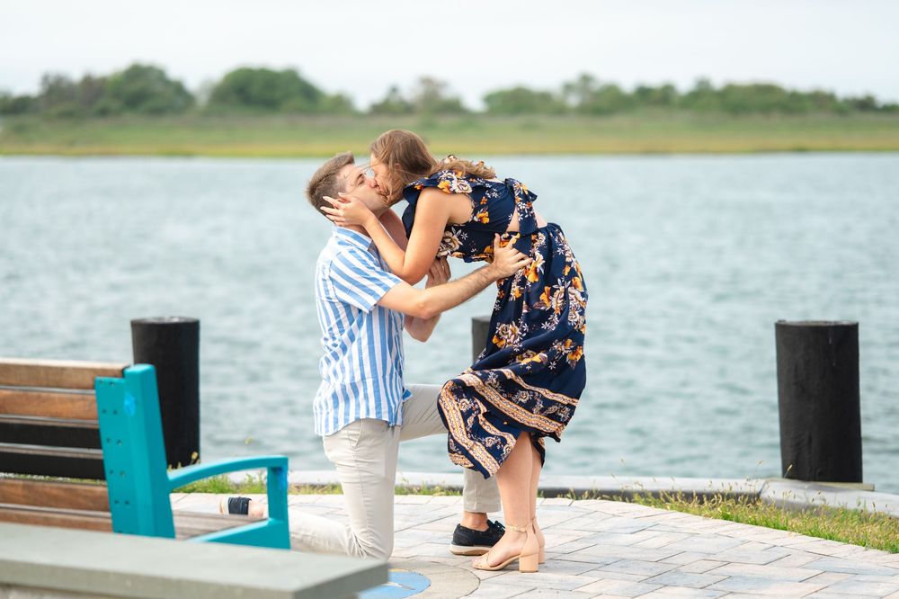Two people share a tender moment on a wooden dock by a serene lake on a sunny afternoon.