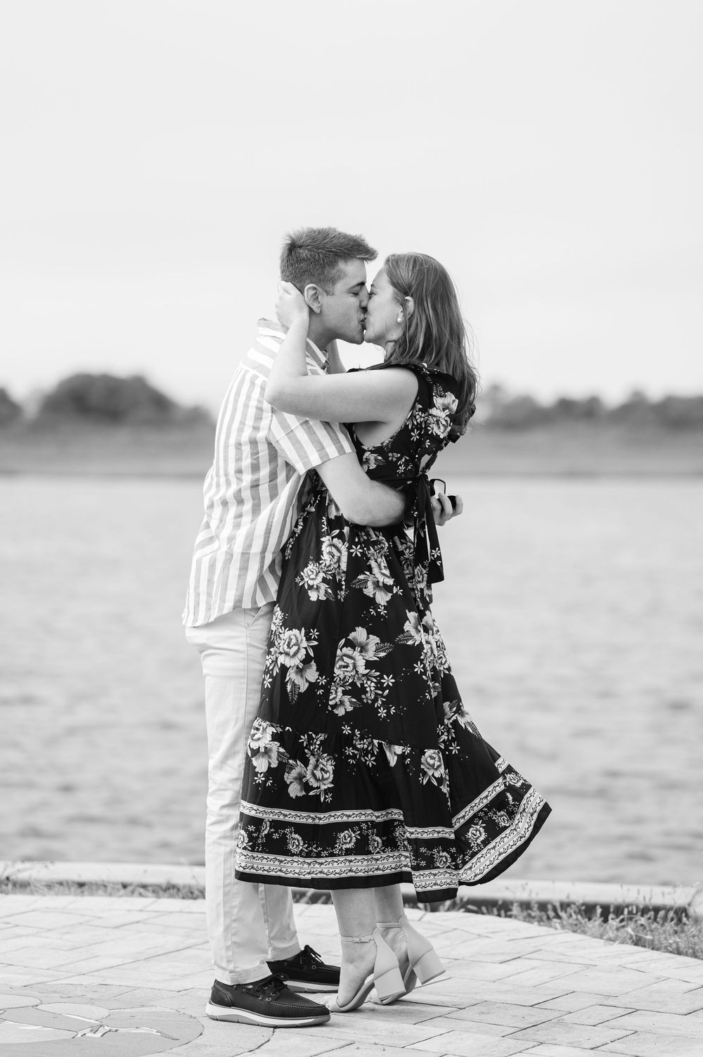 A romantic black and white photo of a couple embracing outdoors, with her wearing a floral dress and him in stripes.
