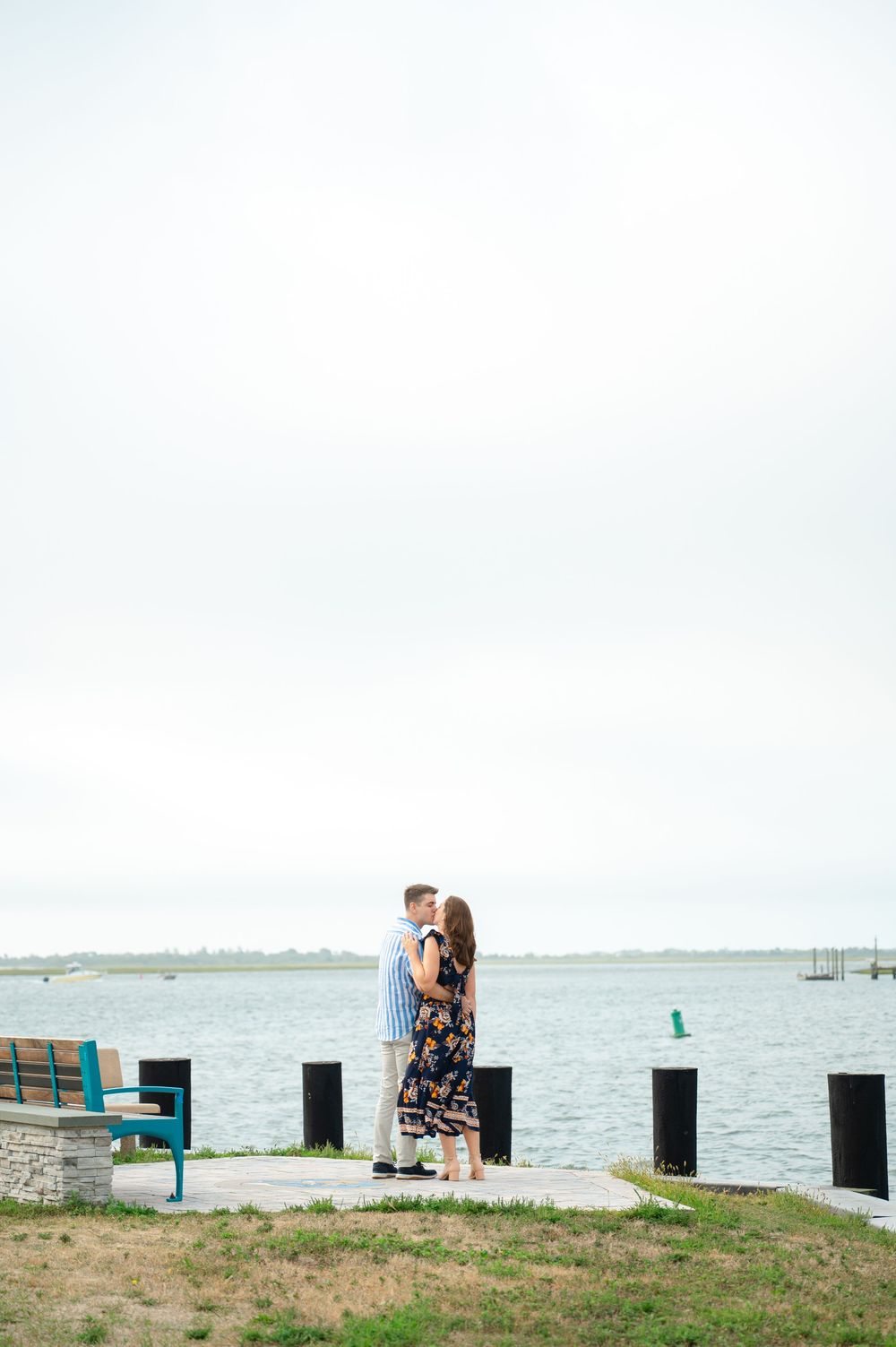 A couple shares a romantic moment by the waterfront with boats and docks in the background in Long Island, NY.