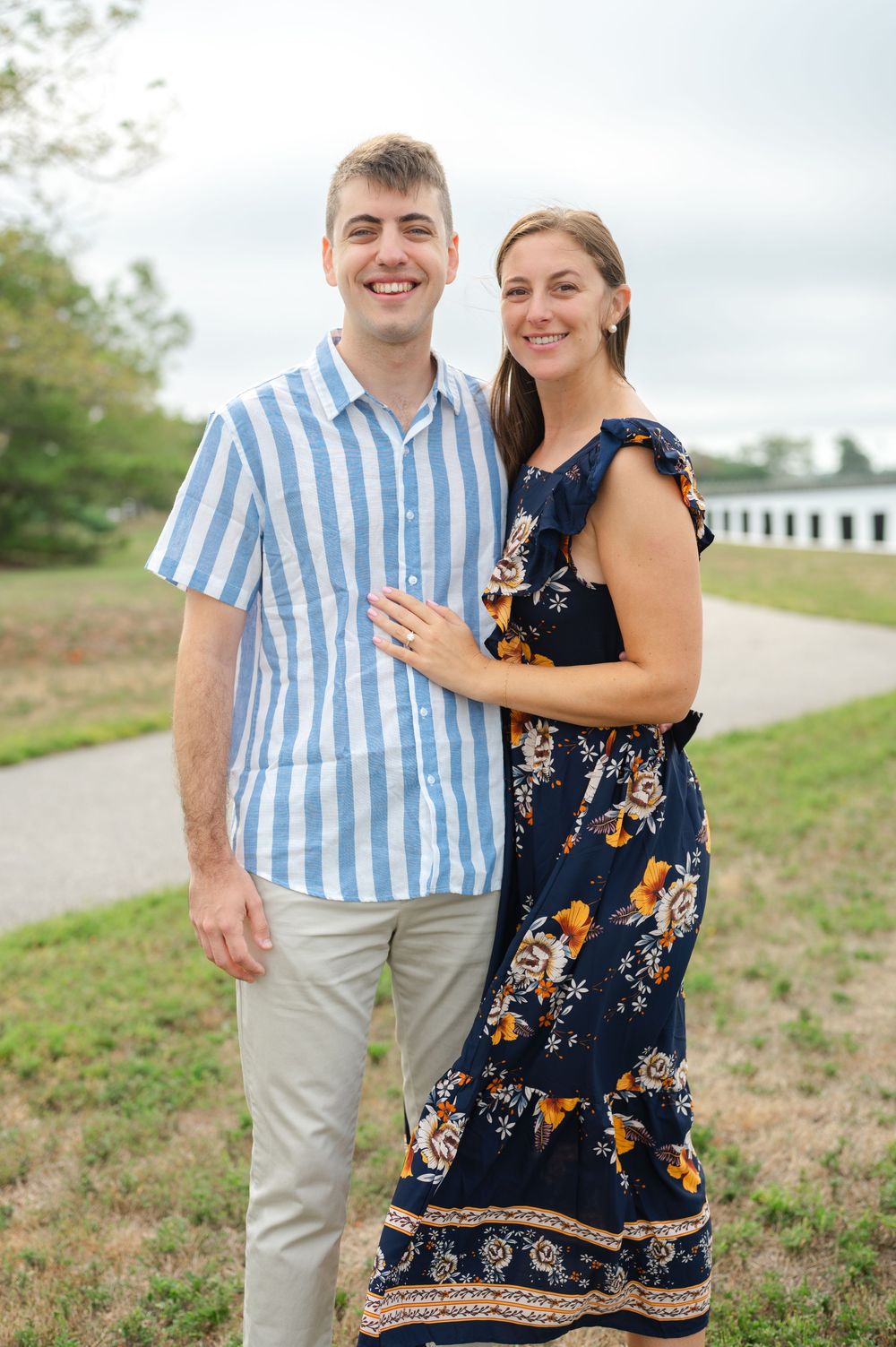 A couple poses together outdoors wearing coordinated summer attire near the water.