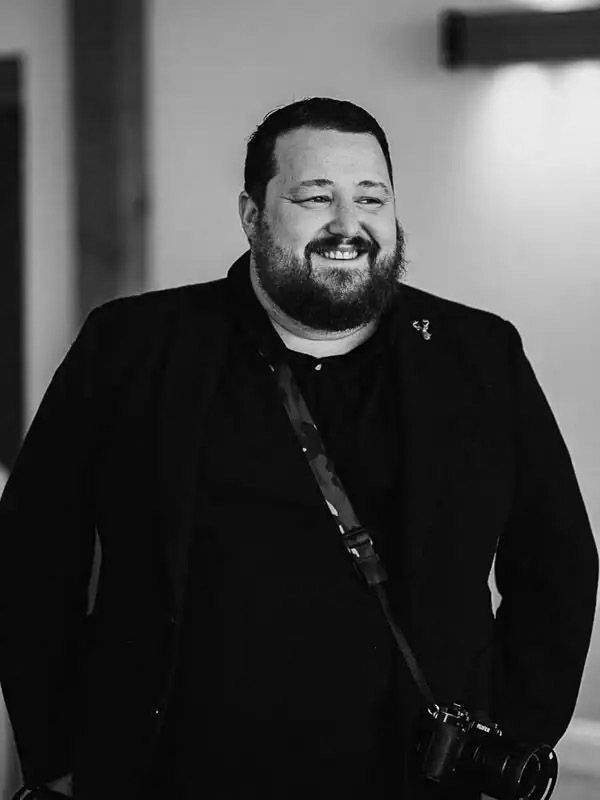 A series of black and white portraits showing a bearded person laughing and smiling in different poses.