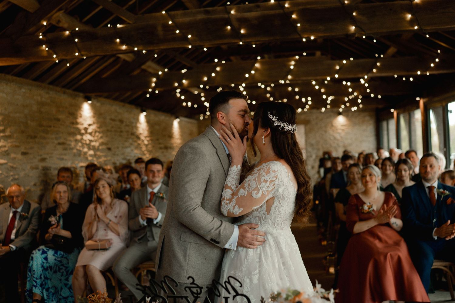 Wedding guests dance together under twinkling string lights at an indoor reception venue.