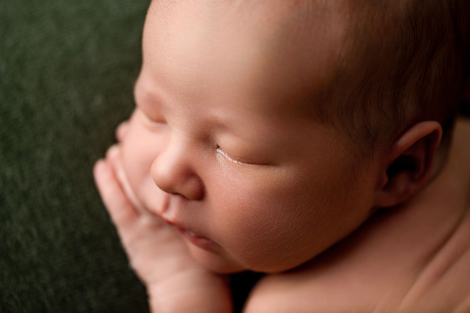 A sleeping newborn baby in soft lighting rests peacefully against a dark green background.