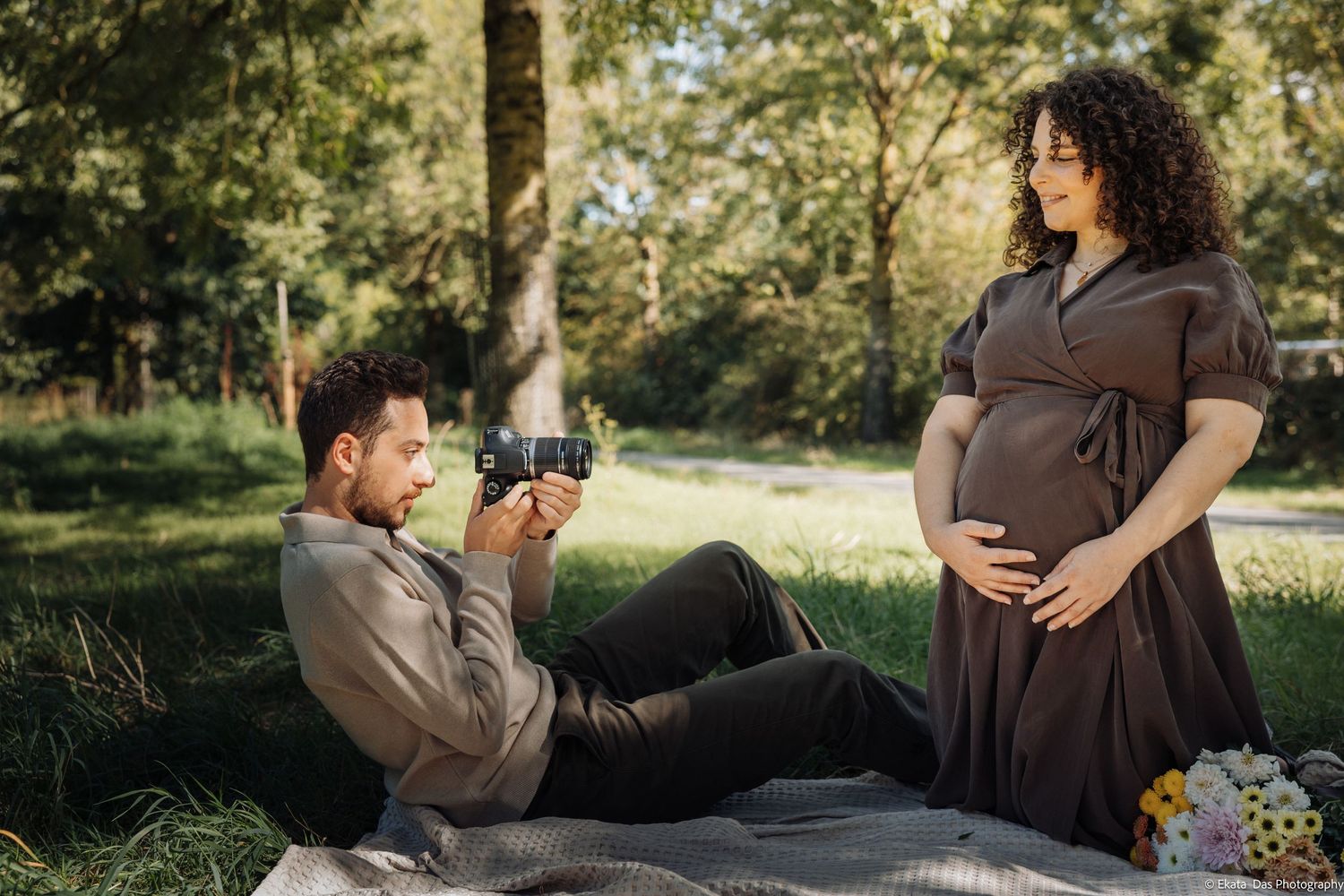 Maternity photos showing close-up of pregnant belly in beige dress against natural backdrop.