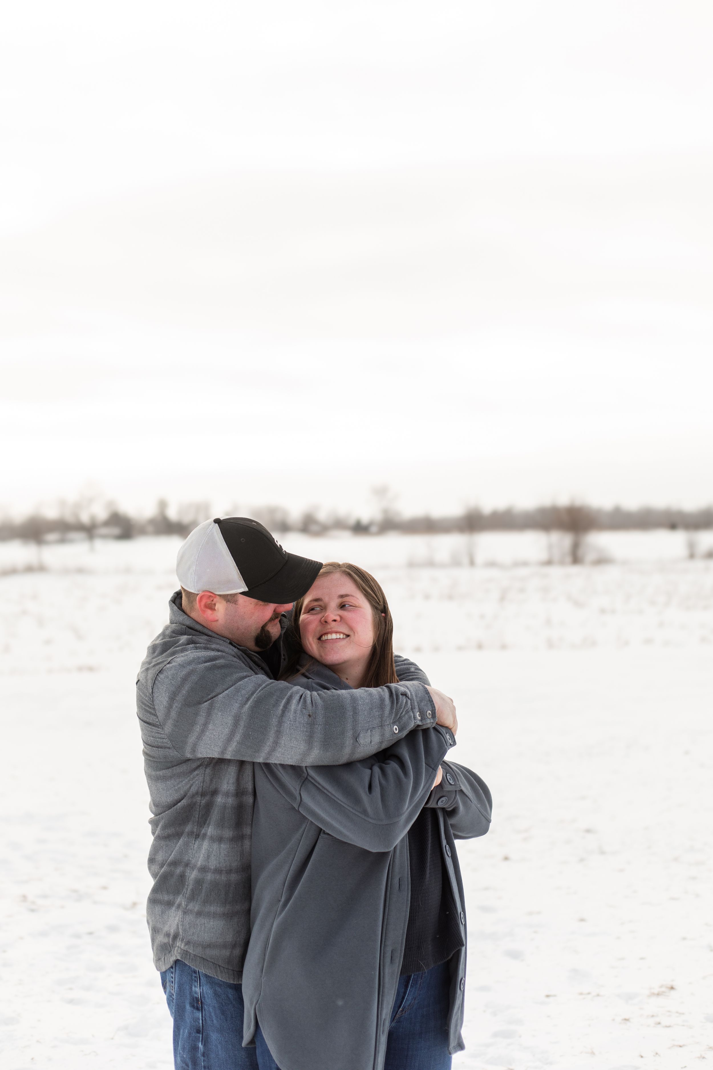 A couple embraces in a snowy winter landscape wearing casual gray clothing and sharing an intimate moment.