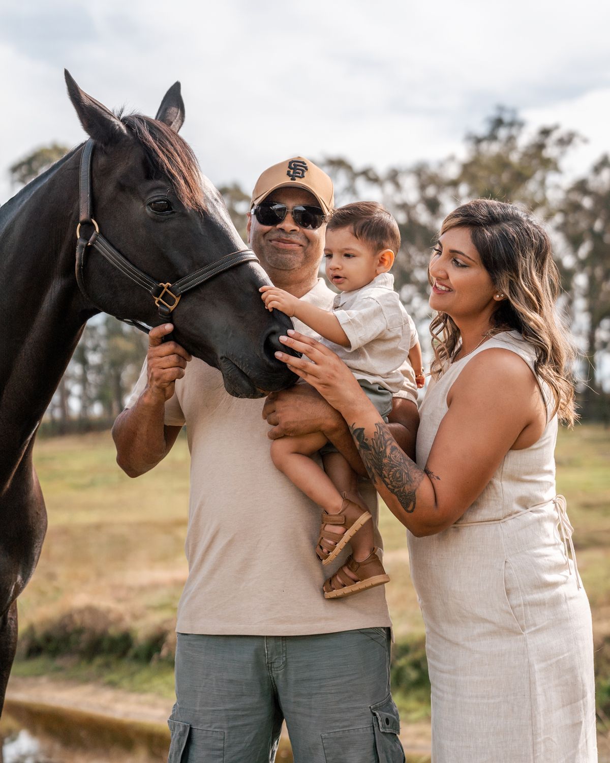 A family stands together petting a large black horse on a sunny day in a rural setting in Rouse hill mothers day photoshoot Sydney