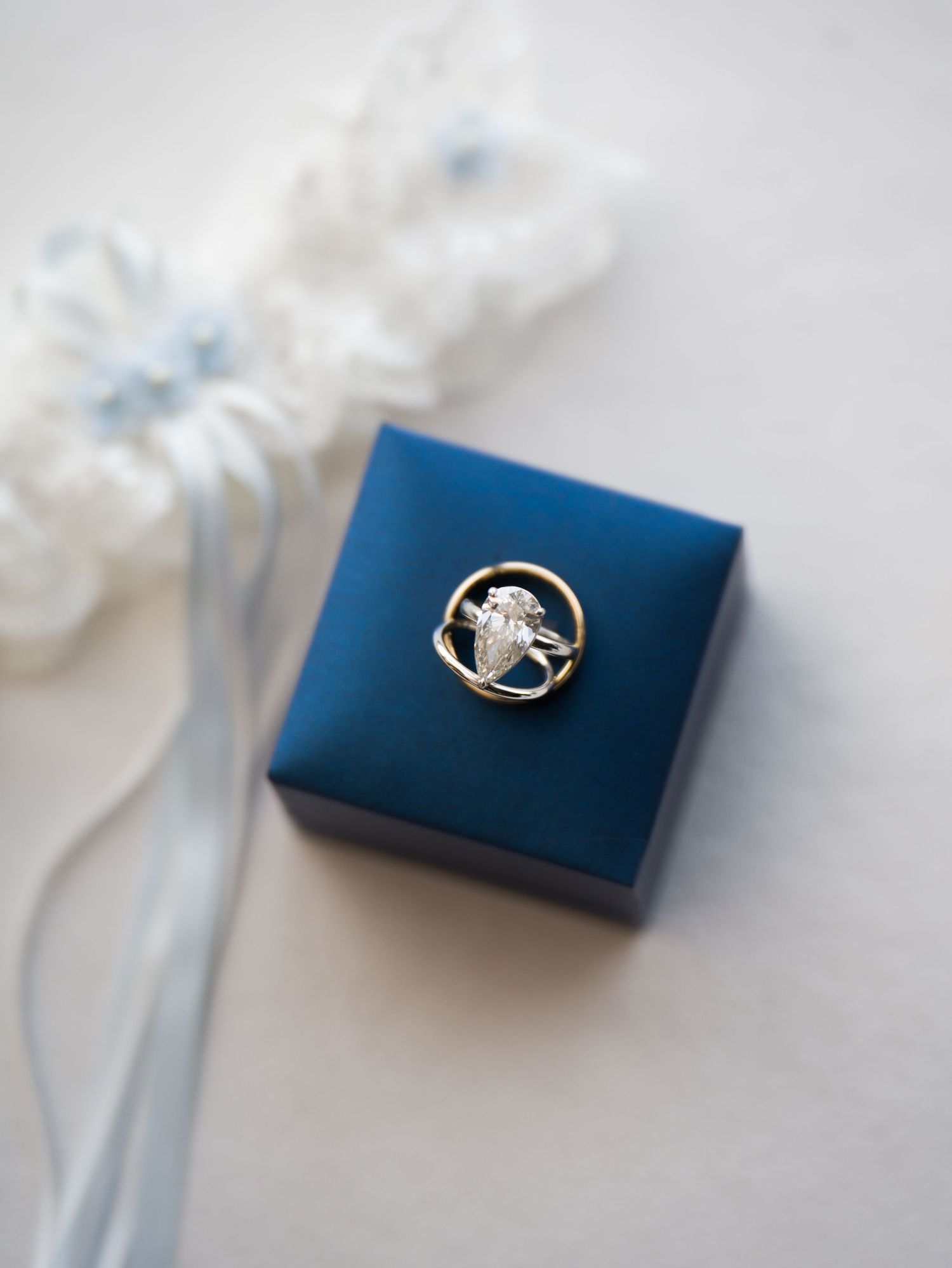 A silver ring with a blue sapphire stone sits atop a navy blue ring box against a white textured background.