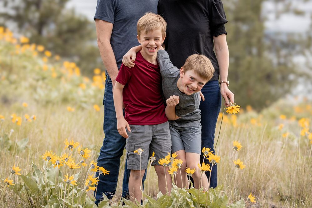 Two young boys laughing together in a field of yellow wildflowers with parents.