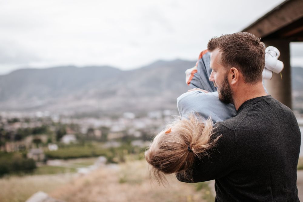 Father holding young child overlooking a mountain valley on a cloudy day.