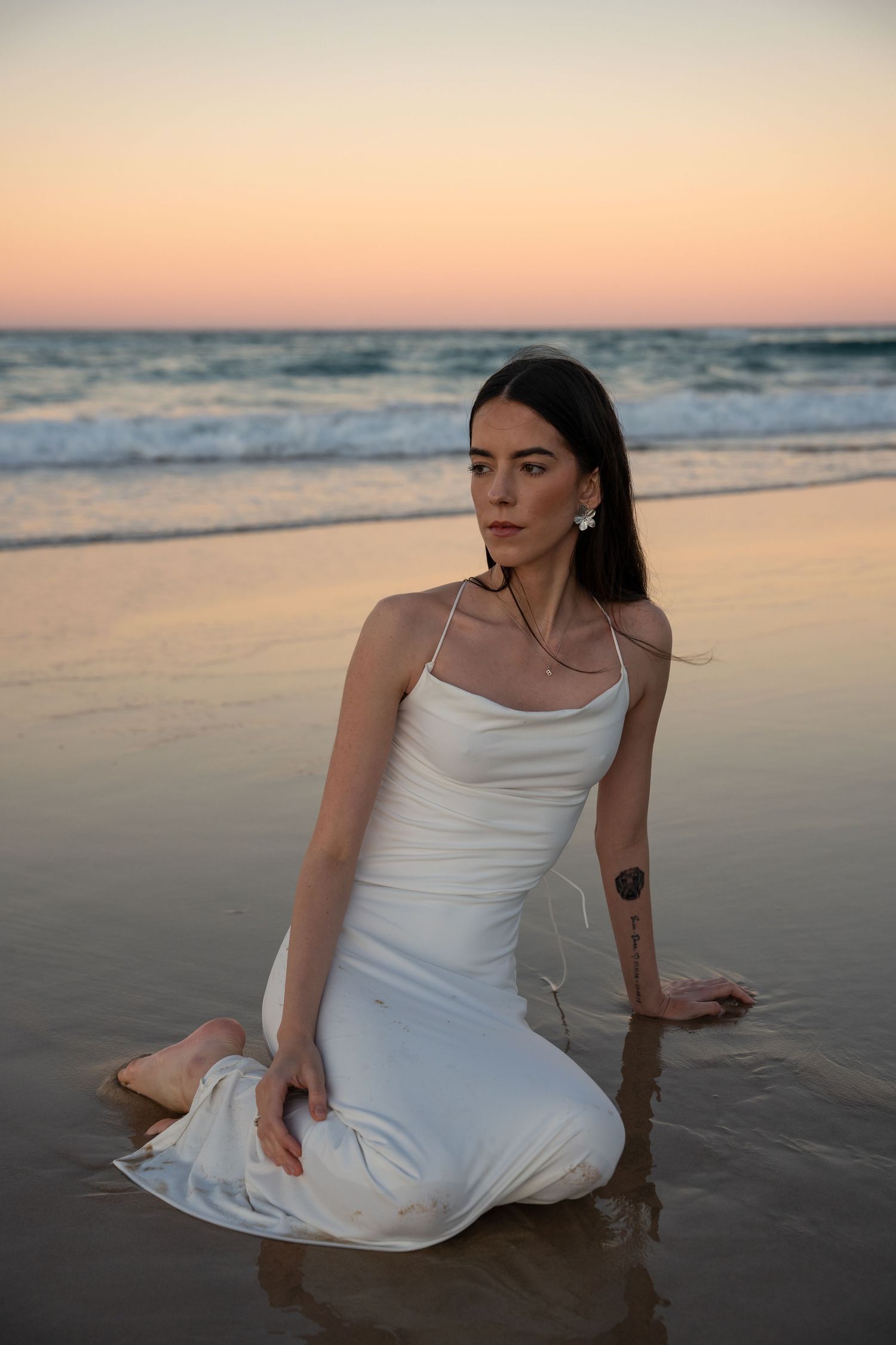 Person in white dress poses gracefully on beach at sunset.